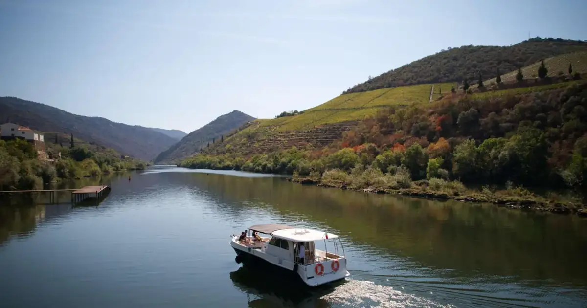 A small cruise boat on the Douro River below terraced vineyards in the wine country