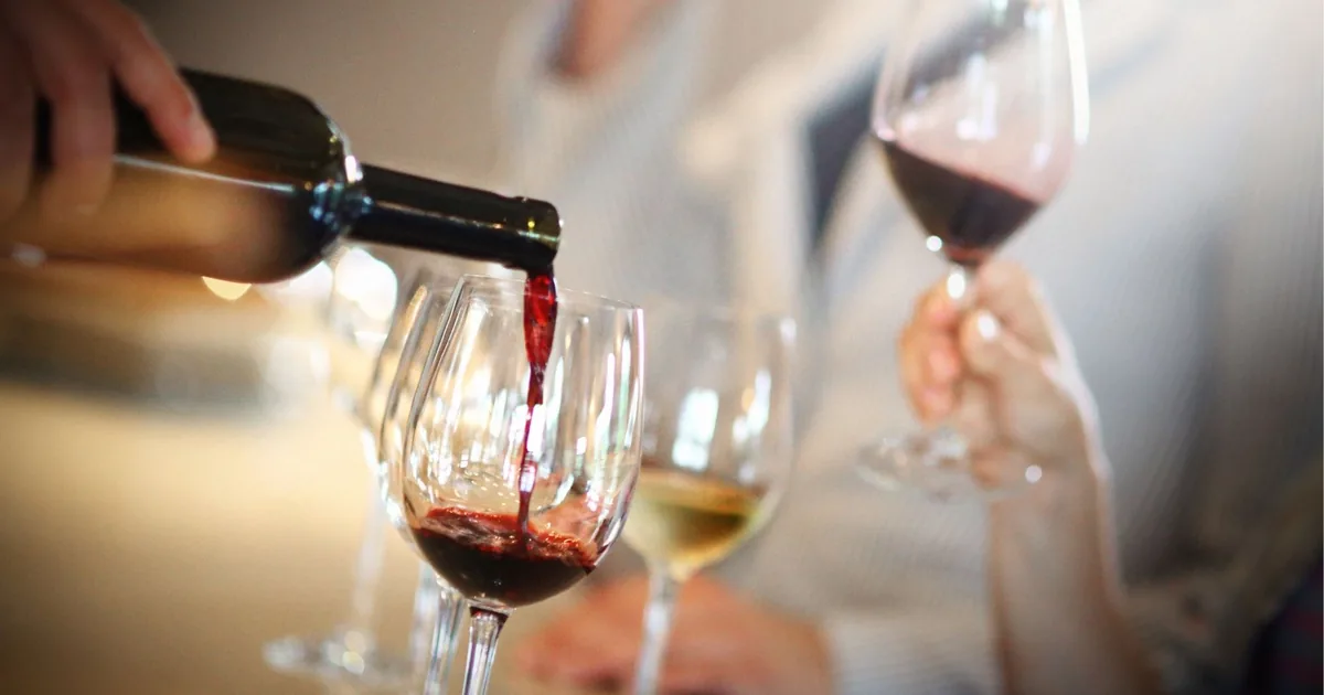 Wine being poured into tasting glasses at a Douro Valley winery, with a white wine and a red already on the table
