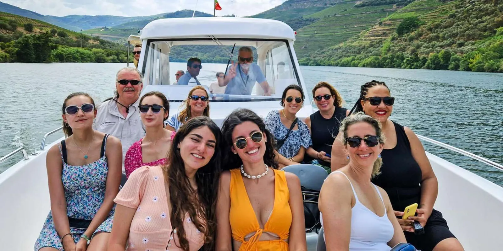 Small group posing together on the Douro River boat cruise, with vineyard hills behind
